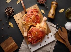 Raw chicken drumsticks seasoned on a wooden board, accompanied by salt and peppercorns, viewed from the top. photo