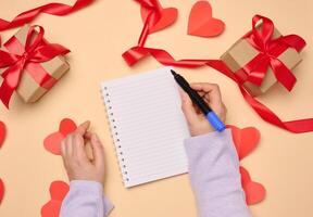 Open notebook with empty white sheets and gift boxes around on a yellow background, top view. photo