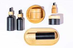 Set of cosmetic products in black and bamboo glass package. Beauty oil in dropper bottle and jars with cream for healthy skin. Unbranded package for cosmetics promotion. Knolling style, top view photo