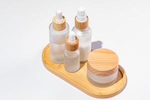 White frosted glass cosmetics bottles and jars with pamboo lids on bamboo tray on white background. Autumn fall beauty products set. photo