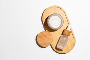 Natural cosmetics in white glass packaging on bamboo tray on white background. Open cream jar and dropper bottle with serum. SPA organic beauty products set. Skin care concept. photo