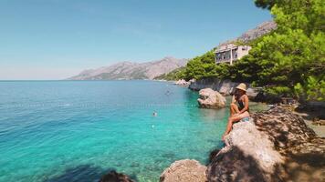 kvinna på klippig strand med grön tall träd och kristall klar hav vattnen. kontemplativ flicka njuter natur landskap i kroatien. video