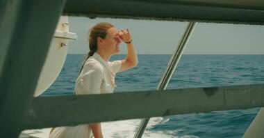 een reflecterende blik van een vrouw van een zee schip. de azuur horizon boeit net zo ze leunt Aan de traliewerk van jacht gedurende zomer reis. video