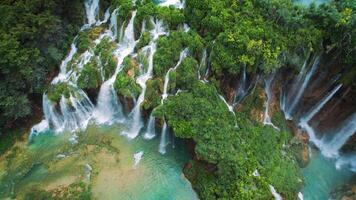 Cascades of waterfalls flow in green tropical forest. River streams falling down. Aerial top down view of lake in spring mountain forest. video