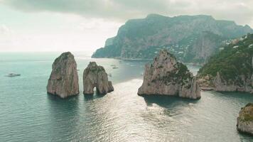 szenisch Küste geschmückt mit ikonisch Meer Stapel faraglioni gegen dunstig Himmel. das felsig Wächter Stand bewachen Über das glitzernd Bucht, schaute Über durch entfernt Berge. Capri, Italien. video