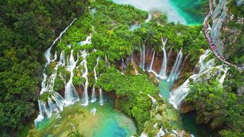 folkmassan av turister besök känd plitvice vattenfall i kroatien. berg strömmar strömma in i en sjö med azurblå klar vatten. video