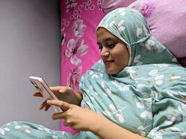 Jakarta, Indonesia. December 21, 2023. A woman wearing a hijab is lying on a bed photo