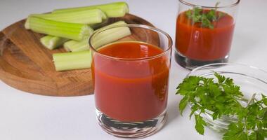 des lunettes de tomate jus sur une blanc tableau. le main met une verre de tomate jus sur le tableau. en bonne santé et végétarien nourriture concept. ultra 4k video