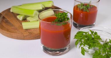 Glasses of tomato juice on a white table. The hand puts a glass of tomato juice on the table. Healthy and vegetarian food concept. Ultra 4K video