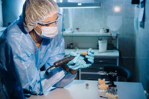 un dental técnico en protector ropa es trabajando en un protésico diente en su laboratorio foto