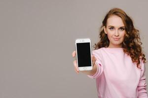 Fashionable girl with a smartphone on the background. Stands and shows the smartphone photo