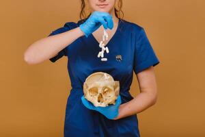 A pretty young doctor pours vitamin capsules into a human skull. The doctor pours pills on the background. photo