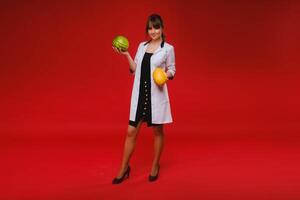 a female doctor nurse in a white coat with fruit in her hands poses on a red background, melon, watermelon, photo