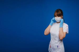 A doctor girl stands in a medical mask on an isolated blue background photo