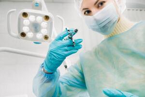 A masked dentist holds an injection syringe for a patient in the office photo