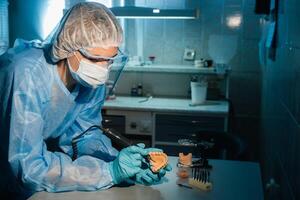 A masked and gloved dental technician works on a prosthetic tooth in his lab photo