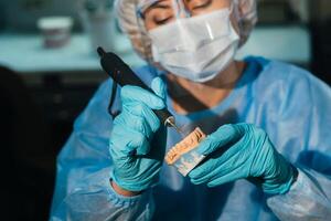 un enmascarado y enguantado dental técnico trabajos en un protésico diente en su laboratorio foto