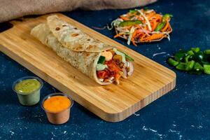 chickpea paneer Chicken shawarma Wrap with salad dip and sauce isolated wooden board side view of fastfood photo