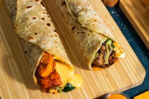 Melt Cheese Paneer Wrap, Chicken Afghani Kebab shawarma Wrap with salad dip and sauce isolated wooden board side view of fastfood photo