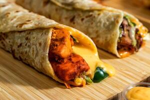 Melt Cheese Paneer Wrap, Chicken Afghani Kebab shawarma Wrap with salad dip and sauce isolated wooden board side view of fastfood photo