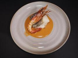 Baked Black Cod Fillet with Argentinian Prawn served in a dish isolated on dark background top view photo