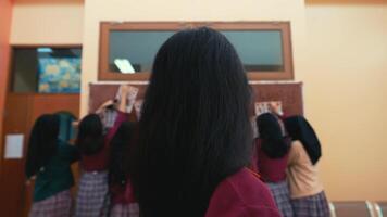 posteriore Visualizza di studenti nel uniforme raccolta mani nel un' aula ambientazione, indicando partecipazione o segreteria un' domanda. video