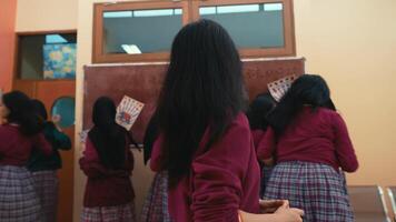 posterior ver de un estudiante con largo pelo en un salón de clases configuración, con compañeros interactuando en el antecedentes. video