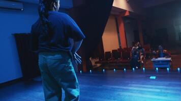 Rear view of a person with a ponytail standing in a dimly lit blue room, looking to the side. video