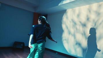 Dynamic dance performance with shadow play in a blue-lit room, showcasing movement and expression. video