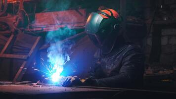 Young mechanic with a welding machine in an old dirty garage at night. Man in protection doing welding work, hobby video