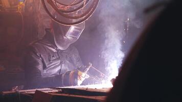 Young mechanic with a welding machine in an old dirty garage at night. Man in protection doing welding work, hobby video