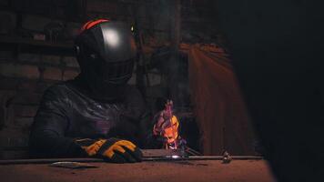 A welder in a protective mask and leather jacket is welding in his atmospheric workshop. Low key. Real time video