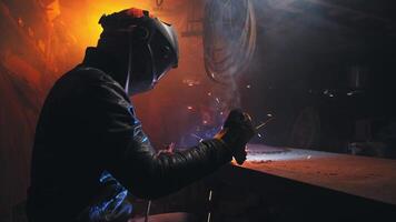 Young mechanic with a welding machine in an old dirty garage at night. Man in protection doing welding work, hobby video