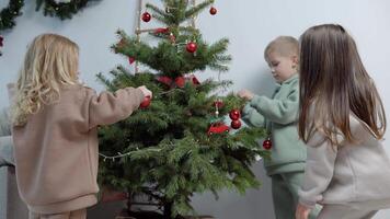 dulce niños en elegante casual trajes Decorar un Navidad árbol video