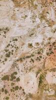 Descending above the rocky landscape with some scarce greenery. Bare dry ground of Travertine Hot Springs from top view. Vertical video