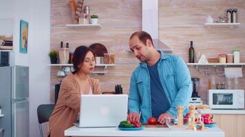 Couple preparing healthy salad in kitchen reading online recipe. Husband and wife cooking recipe food. Happy healthy together lifestyle. Family searching for online meal. Health fresh salad video