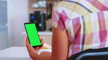 Woman using smartphone with chroma key in kitchen during breakfast. Green screen chroma mock up isolated mockup background ready to be replaced with your text, logo or advertisement. Using internet, social networks and browsing video