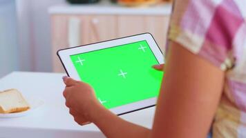 femme navigation sur tablette ordinateur avec vert écran dans cuisine. vert écran chrominance moquer en haut isolé maquette Contexte prêt à être remplacé avec votre texte, logo ou publicité. en utilisant l'Internet, social réseaux et navigation video