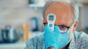 Medical assistance checking senior man body temperature using infrared thermometer in kitchen. Social worker checking on vulnerable persons for disease spreading prevention video