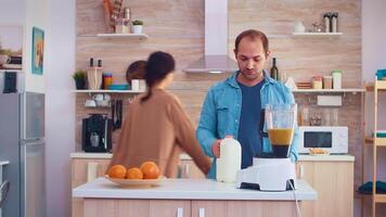 homem derramando leite dentro liquidificador para fresco e saudável batido para ele e alegre esposa. alegre família fazer juntos orgânico saudável fresco nutritivo saboroso suco para café da manhã a partir de fresco frutas enquanto em uma dieta. video