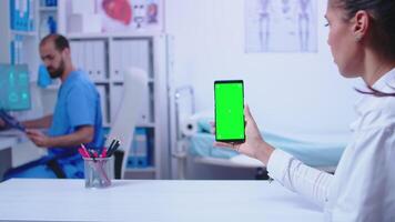 läkare i vit täcka innehav smartphone med grön skärm i sjukhus skåp. sjuksköterska bär medicinsk blå enhetlig. video