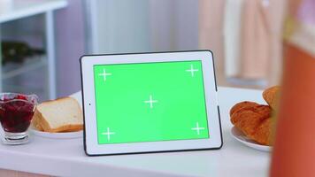 Jeune femme dans cuisine en utilisant tablette ordinateur avec vert moquer en haut. vert écran chrominance moquer en haut isolé maquette Contexte prêt à être remplacé avec votre texte, logo ou publicité. en utilisant l'Internet, social réseaux et navigation video