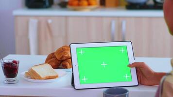 Woman searching recipe on table computer with green mockup in kitchen. Delicious french pastry. Green screen chroma mock up isolated mockup background ready to be replaced with your text, logo or advertisement. Using internet, social networks and browsing video