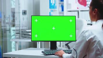 hembra médico trabajando en computadora con verde pantalla en privado clínica gabinete. asistente en uniforme. médico en blanco Saco trabajando en monitor con croma llave en clínica gabinete a cheque paciente diagnosticar. video