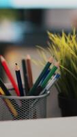 Vertical video Focus on desk belongings in modern office with notebook in blurry background showing business diagram and figures, close up. Pencil holder, mini house plant, empty coffee mug and graphs on laptop