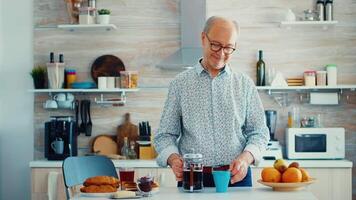 senior man häller varm kaffe från franska Tryck i kök under frukost. äldre person i de morgon- njuter färsk brun Kafé espresso kopp koffein från årgång mugg, filtrera koppla av förfriskning video