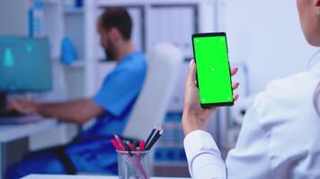 Medical physician holding smartphone with mockup in hospital cabinet while male nurse is working on computer. Healthcare specialist in hospital cabinet using smartphone with mockup. video