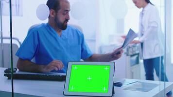 Assistant giving doctor patient x-ray and tablet pc with green screen display. View of tablet computer with chroma key through glass wall in hospital. video