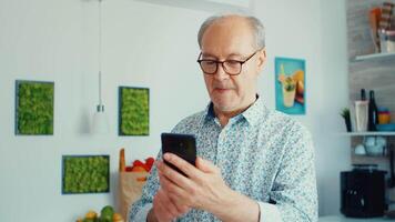 Happy grandfather listening music and dancing while having breakfast in kitchen wearing glasses Relaxed elderly senior dancing, fun lifestyle with modern technology video