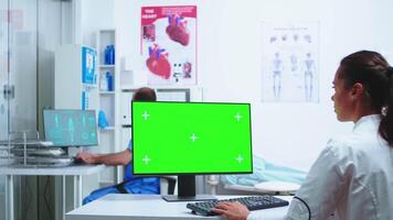 enfermeira consultando com médico dentro hospital gabinete enquanto trabalhando em computador com cópia de espaço verde tela disponível. Área de Trabalho com substituível tela dentro médico clínica enquanto médico é verificação paciente radiografia para diagnosticar. video